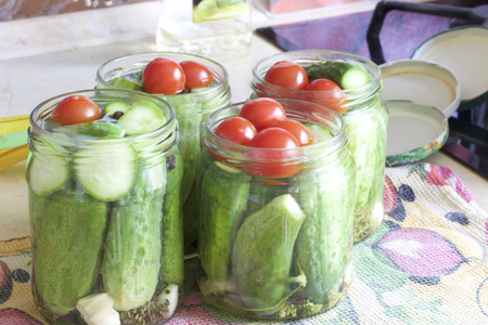 Pickling cucumbers and tomatoes. Cucumbers, tomatoes and spices packed in glass jars. Flooded with marinade. Stocking up for winter.の写真素材