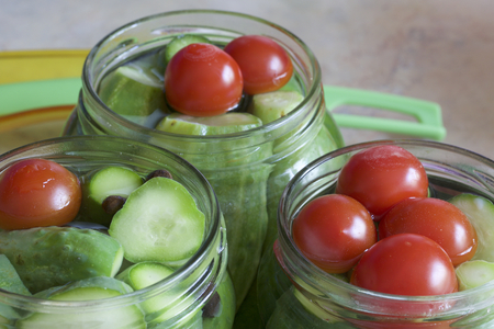 Pickling cucumbers and tomatoes. Cucumbers, tomatoes and spices packed in glass jars. Flooded with marinade. Stocking up for winter.の写真素材