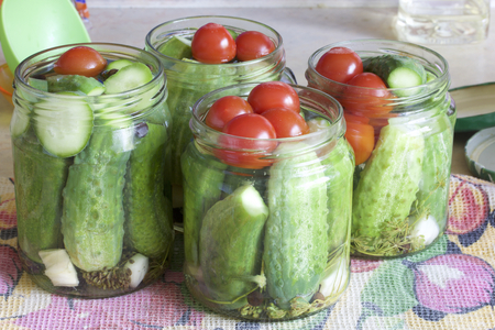 Pickling cucumbers and tomatoes. Cucumbers, tomatoes and spices packed in glass jars. Flooded with marinade. Stocking up for winter.の写真素材