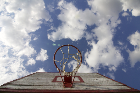 Basketball board with a net. Old, wooden planks. Painted. Located on a background of blue sky with clouds. Sport games in the yard. View from under the ring.の写真素材