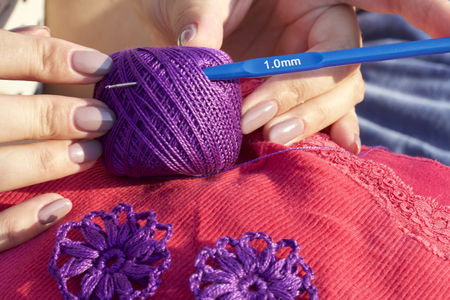 The woman knits earrings in the shape of a flower. Ornament from silk yarn, crochet. Self-made...