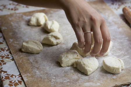 The process of preparation of Ukrainian dumplings. Girl rolled out dough, cut into pieces and mold dumplings. Dough, flour and tools lying on a cutting board.の写真素材