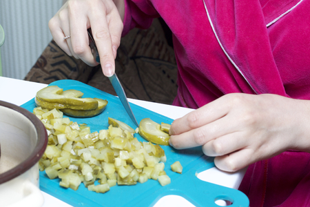 Vegetable salad. Russian recipes.  Cooking Stages. Cooking ingredients: Woman cuts vegetables on board pickled cucumbers.の写真素材