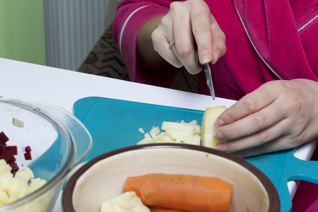 Vegetable salad. Russian recipes.  Cooking Stages. Woman slices boiled potatoes into cubes. A kitchen knife on a cutting board. Nearby stands a pan with vegetable cutting.の写真素材