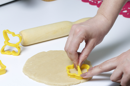 Preparation of baking cookies at home. On the table lay the rolled dough and rolling pin wood. Near plastic molds to make the dough a beautiful shape. Woman pushes the dough molds.の写真素材