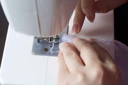 A woman works on a sewing machine. She sews the curtains on the window.