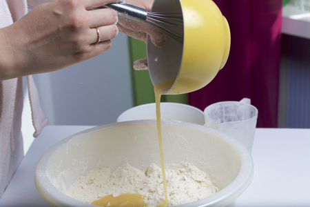 Pie with stuffing from cottage cheese and apple jam. Stages of preparation. A woman pours a beaten egg and sugar into the mixed butter and flour to make a dough.の写真素材