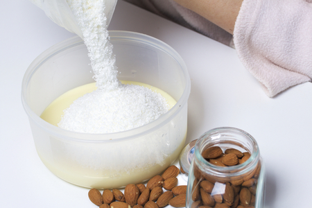 Walnut almonds. In a glass jar, scattered on the table. Next to the container with condensed milk into which a woman is pouring coconut shavings. On a white background.の写真素材