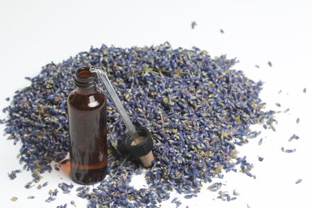 Dried flowers of lavender. A vial of dark glass with a pipette, sprinkled with a cluster of inflorescences of lavender. On a white background.の写真素材