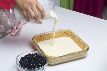 The woman adds the filling to the biscuit.  Delicate cheesecake with blueberries. Ingredients: cookies and lemon stand on the table.の写真素材