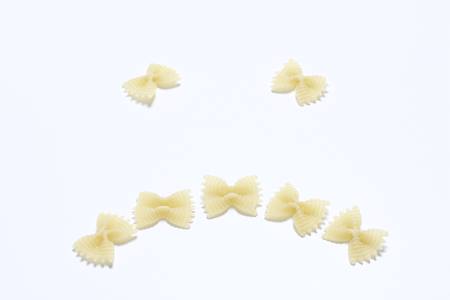 A sad smiley, laid out of pasta on a white surface.の写真素材