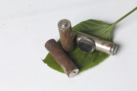 Waste batteries of different types are scattered. Below them a green juicy leaf. On a white...
