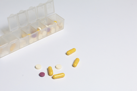 Tablets and pills are spread out into a container for tablets on the days of the week. Medicines of different shapes and colors. Several tablets are scattered around the table.の写真素材