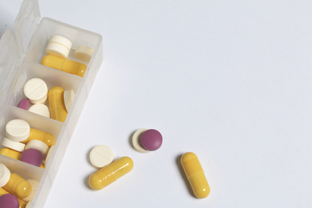 Tablets and pills are spread out into a container for tablets on the days of the week. Medicines of different shapes and colors. Several tablets are scattered around the table.の写真素材