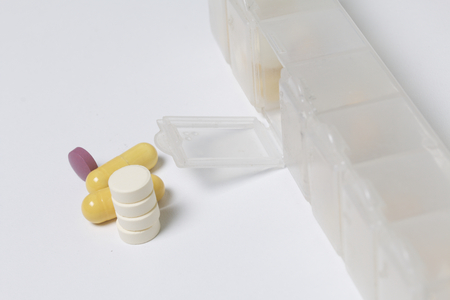 A daily dose of tablets lies near a special container for daily medication. One cell for this day is open, tablets from it lie side by side.の写真素材