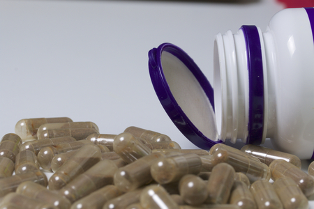 Brown pills are poured on a white surface from a plastic jar.の写真素材