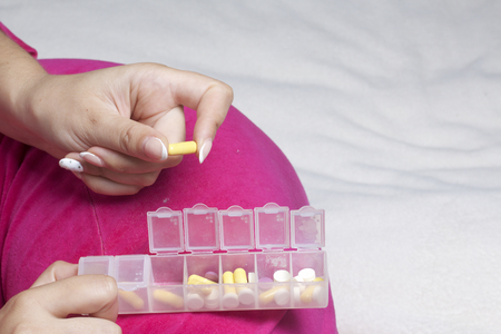 Woman lying in bed taking pills from a special container. Holds a container and a pill.の写真素材