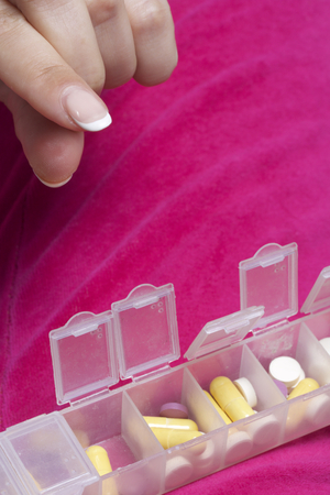 Woman lying in bed taking pills from a special container. Holds a container and a pill.
