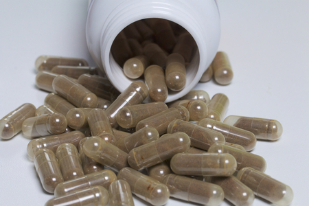 Brown pills are poured on a white surface from a plastic jar.の写真素材