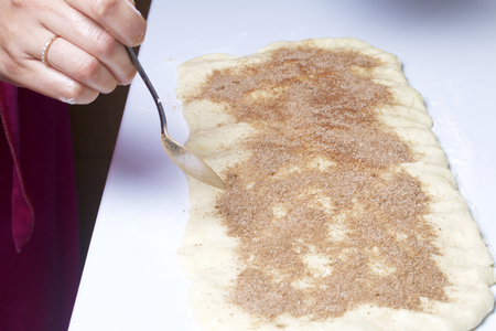 A woman is cooking buns with cinnamon. She rolls the stuffing onto the rolled dough. Mixed sugar and cinnamon.の写真素材