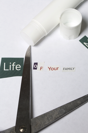 Criminal activity. Preparation of a letter with threats. Letters cut from different editions are pasted onto a white sheet of paper. Next to the letter lie scissors, glue and a few cut but not napped letters.の写真素材