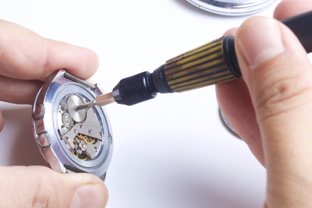 The watch workshop. Repair of old watches. The mechanism of the clock, the screwdriver, which the master makes repairs, is visible. On a white background.の写真素材