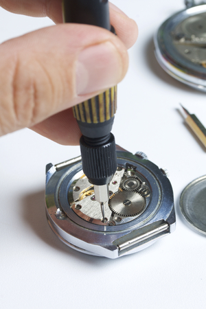 The watch workshop. Repair of old watches. The mechanism of the clock, the screwdriver, which the master makes repairs, is visible. On a white background.の写真素材