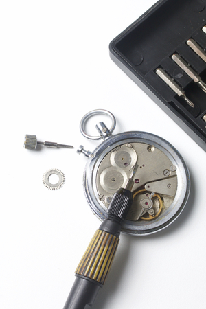 The watch workshop. Repair of old watches. The mechanism of the clock, the screwdriver, which the master makes repairs, is visible. On a white background.の写真素材