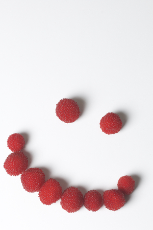 Large red berries are similar to raspberries. In the form of a smiling smiley. On a white...