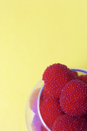 Large red berries are similar to raspberries in a glass vase. On a yellow background. View from above.の写真素材