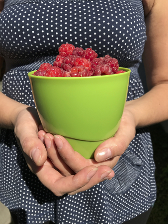 The woman is holding a large mug in front of her with a fresh juicy red raspberry.