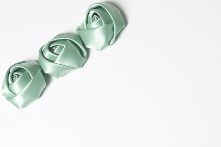 Homemade roses from emerald satin. Are located on the left corner of the frame. On a white background.の写真素材