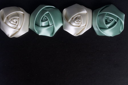Homemade roses from white and emerald satin. Are located on the top of the frame. On a black background.の写真素材