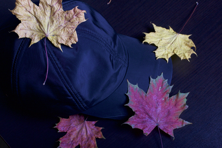 Black sports hat, strewn with autumn fallen leaves. On a dark background.の写真素材