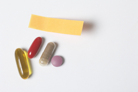 On the white surface of the table lie pills of different colors. Next is a paper sticker with a reminder.の写真素材