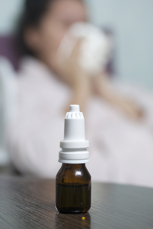 Nasal drops. The bottle is on the table. On the background of a woman who blows her nose in a handkerchief.の写真素材