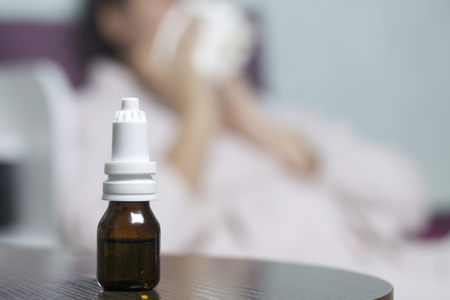 Nasal drops. The bottle is on the table. On the background of a woman who blows her nose in a handkerchief.の写真素材