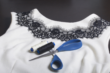 Sewing and dressing. On the dark surface is a white dress with a black ribbon sewn for decoration. There are scissors and coils of thread nearby.の写真素材