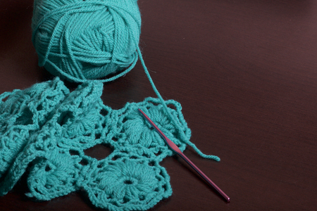 Crochet. On the dark surface of the table lies an unfinished knitted product with knitting needles and a ball of emerald-colored threads.の写真素材