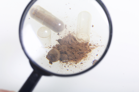 Look through the magnifying glass. The brown pills are scattered over the white surface. One active ingredient is poured from one pill.の写真素材