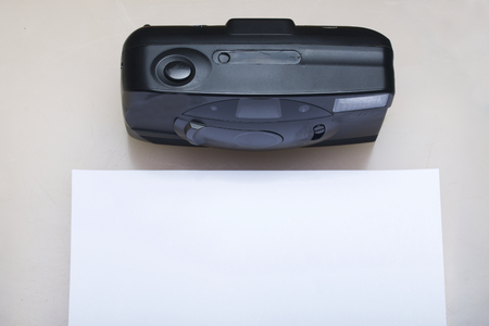 Old semi-automatic camera. Lies on a white surface. Near the photo paper. View from above.の写真素材
