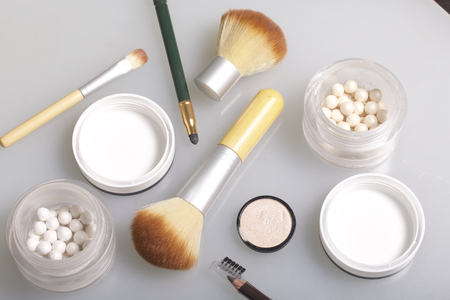 Golden and pearl highlighter in the form of balls in an open jar. Close to the brush for applying cosmetics and cosmetic pencils. On a white background, view from above.の写真素材