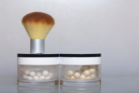 Golden and pearl highlighter in the form of balls in an open jar. Next to it is a cosmetic brush for applying it. On a white background.の写真素材