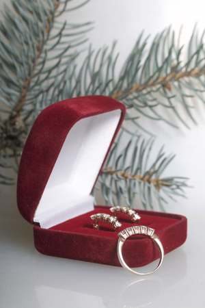 A gift to a loved one. An open velvet box of red color with gold earrings. Nearby is a golden ring....