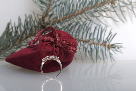 A gift to a loved one. A velvet red pouch. Nearby is a golden ring. On a white background with a spruce branch.の写真素材