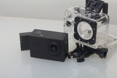 The action camera lies on a white surface. Near the box for underwater shooting and a spare battery.の写真素材