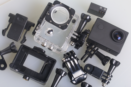 The action camera lies on a white surface. The action camera lies on a white surface. Near the box for underwater shooting, spare battery and other accessories. View from above.の写真素材