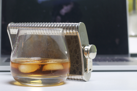 Whiskey with ice in a glass and a flask. Nearby is a laptop. Rest of the day off.の写真素材