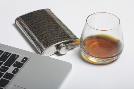 Whiskey in a glass and a flask. Nearby is a laptop. Rest of the day off.の写真素材