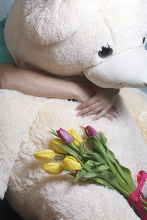 The girl holds a bouquet of yellow and pink tulips. They lie on a large soft toy, which is embraced by a woman.の写真素材